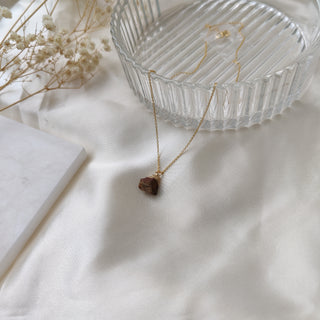 Necklace with a pendant on a white surface with a glass dish and dried flowers.